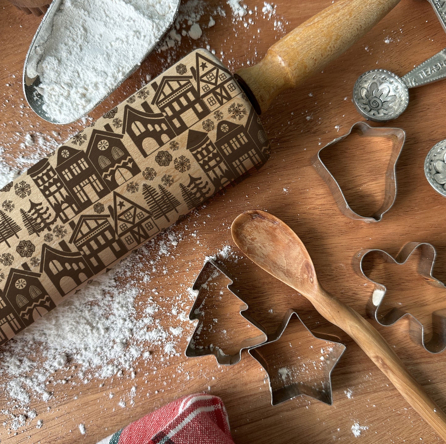 Baking tools including a rolling pin with embossed patterns, cookie cutters, and flour on a wooden surface.