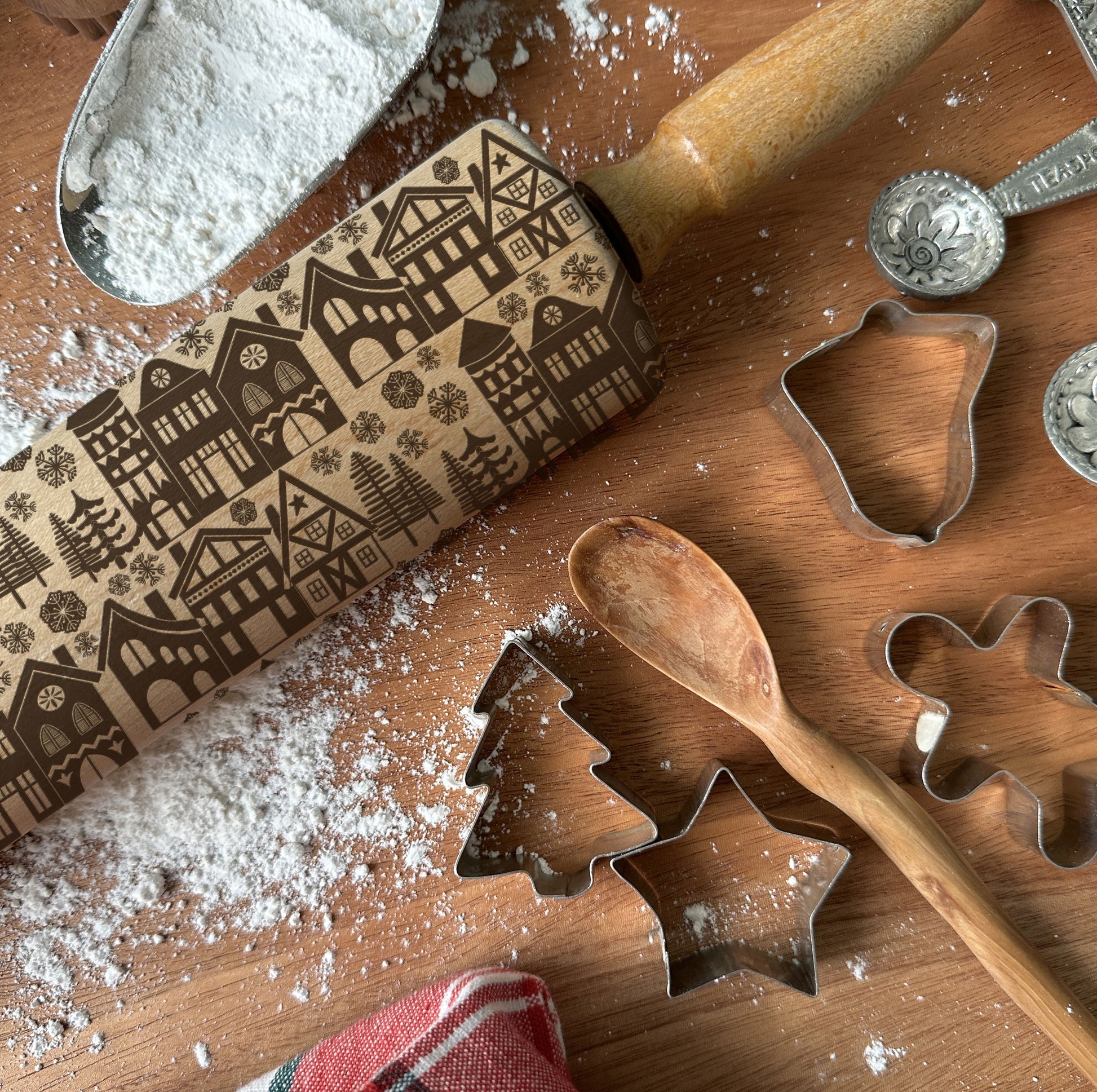 Baking tools including a rolling pin with embossed patterns, cookie cutters, and flour on a wooden surface.
