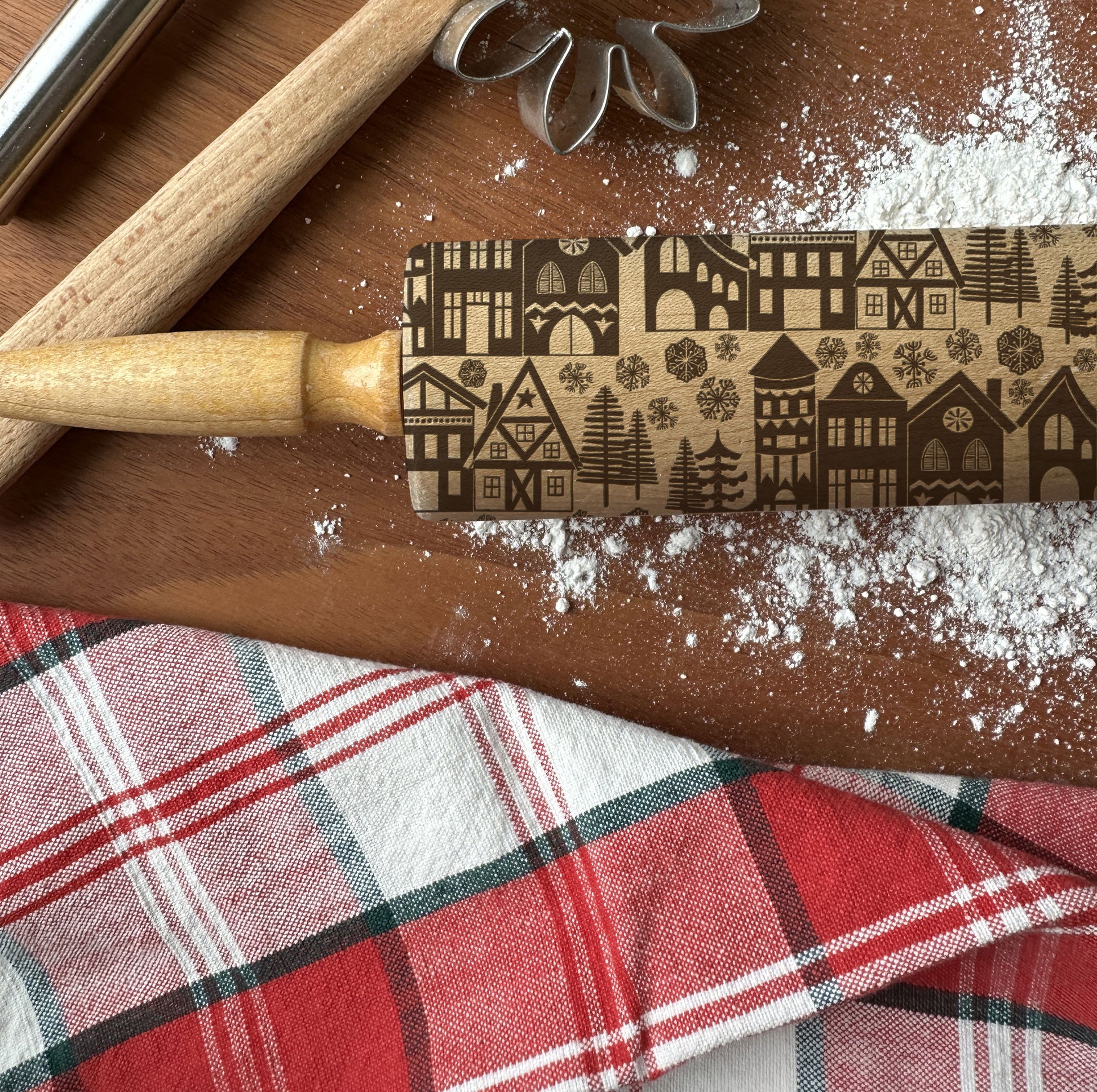 Rolling pin with embossed pattern on a wooden surface with flour and a plaid cloth.