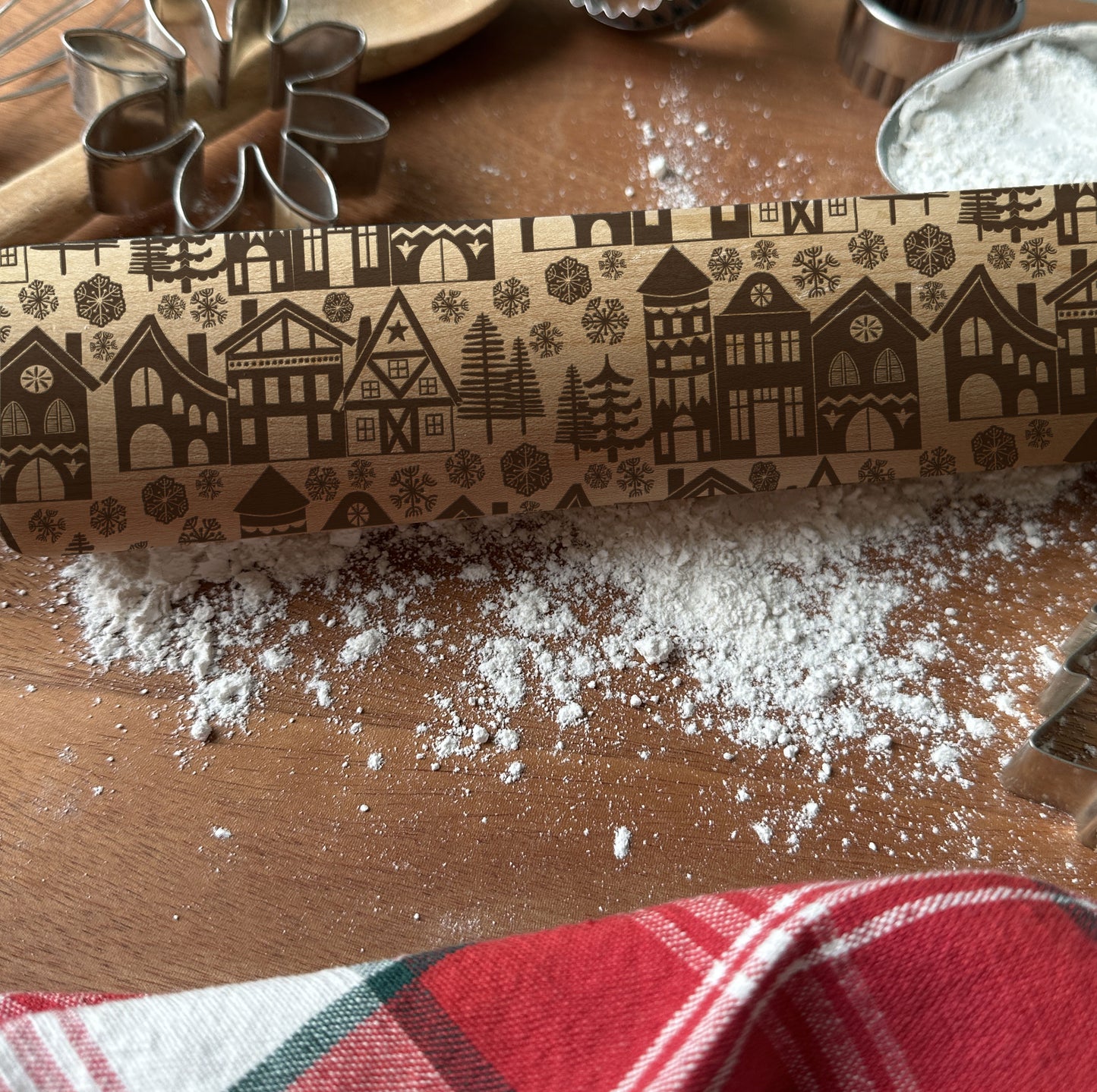 Rolling pin with decorative pattern on a wooden surface with flour and cookie cutters.