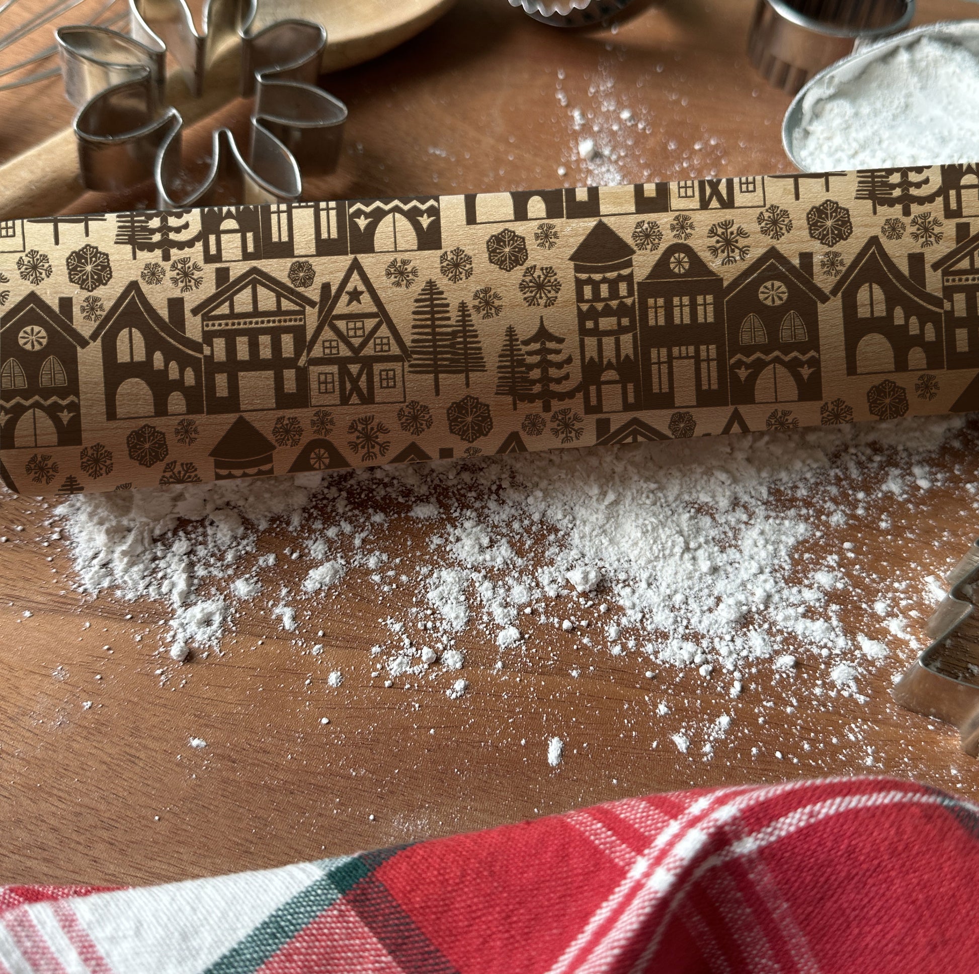 Rolling pin with decorative pattern on a wooden surface with flour and cookie cutters.