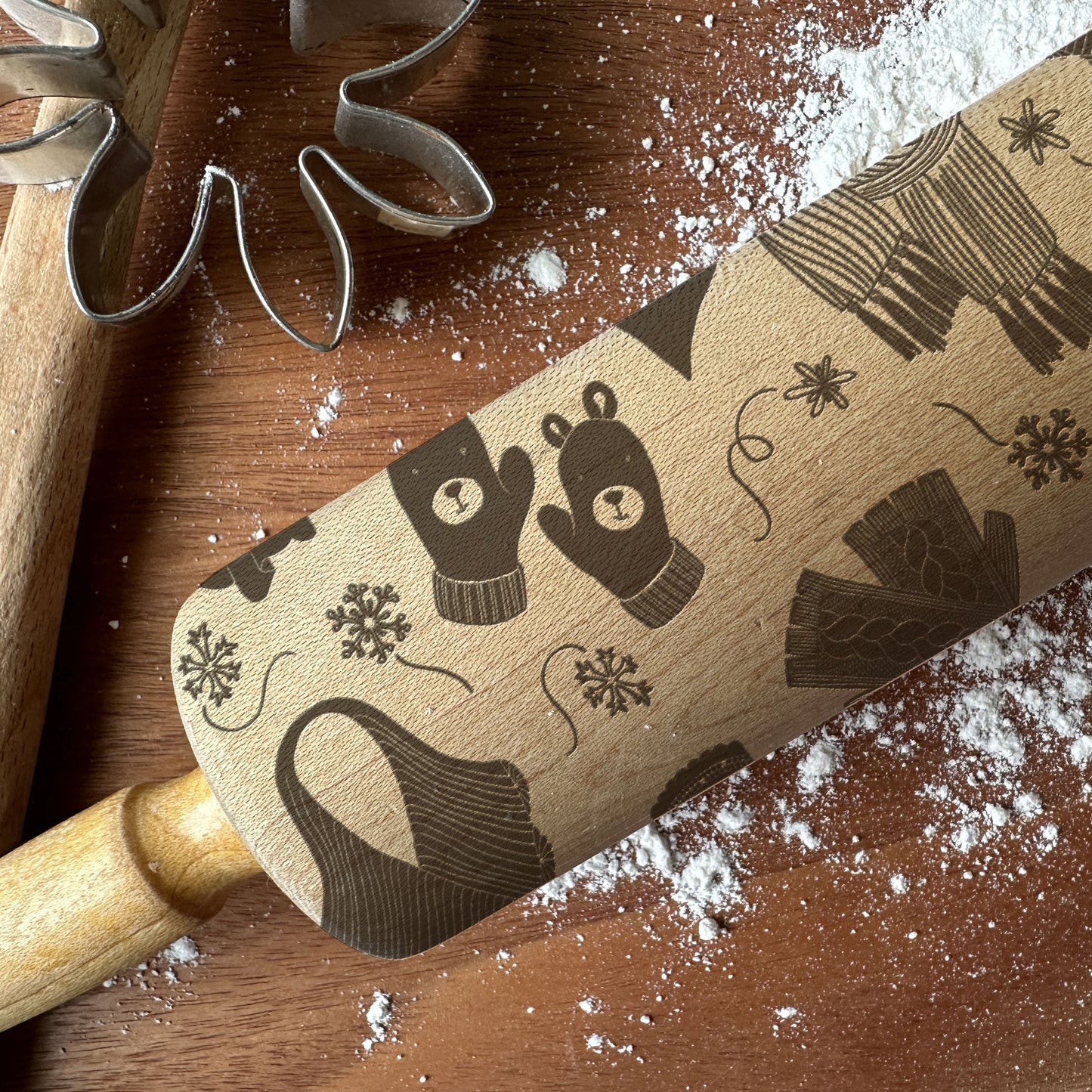 Wooden rolling pin with winter-themed design on a wooden surface with flour.