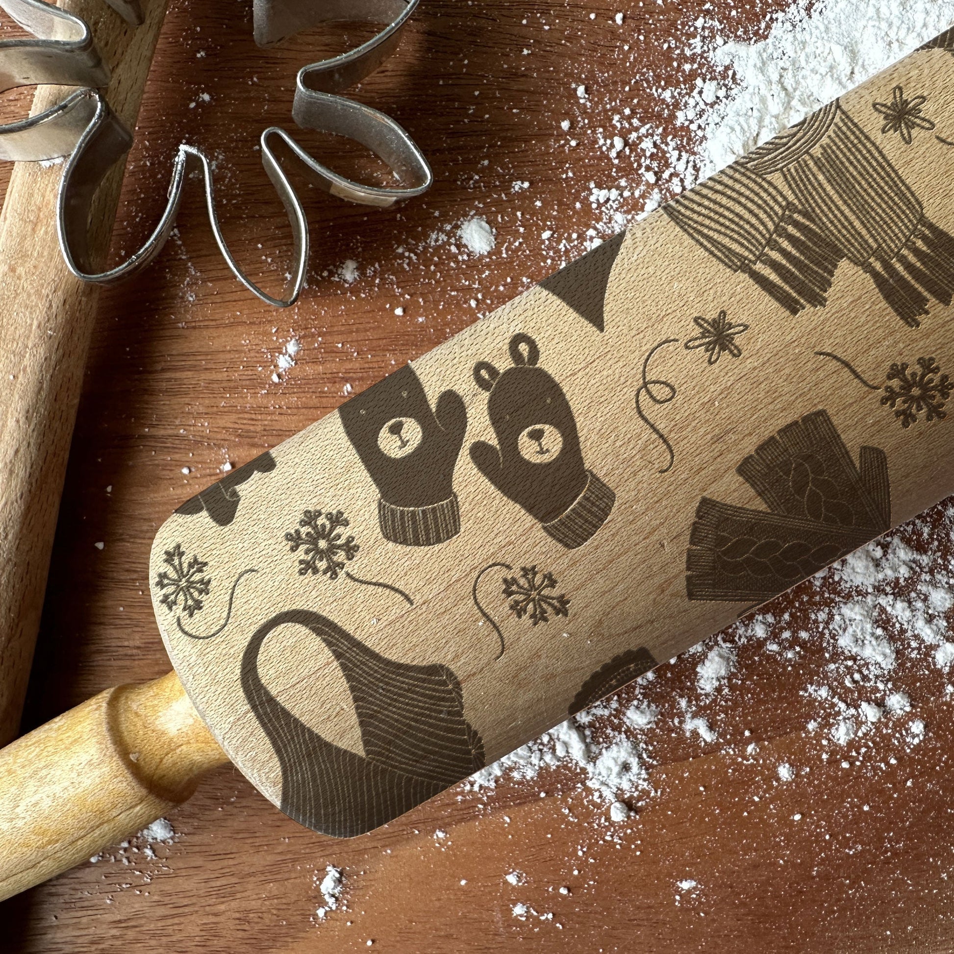 Wooden rolling pin with winter-themed design on a wooden surface with flour.