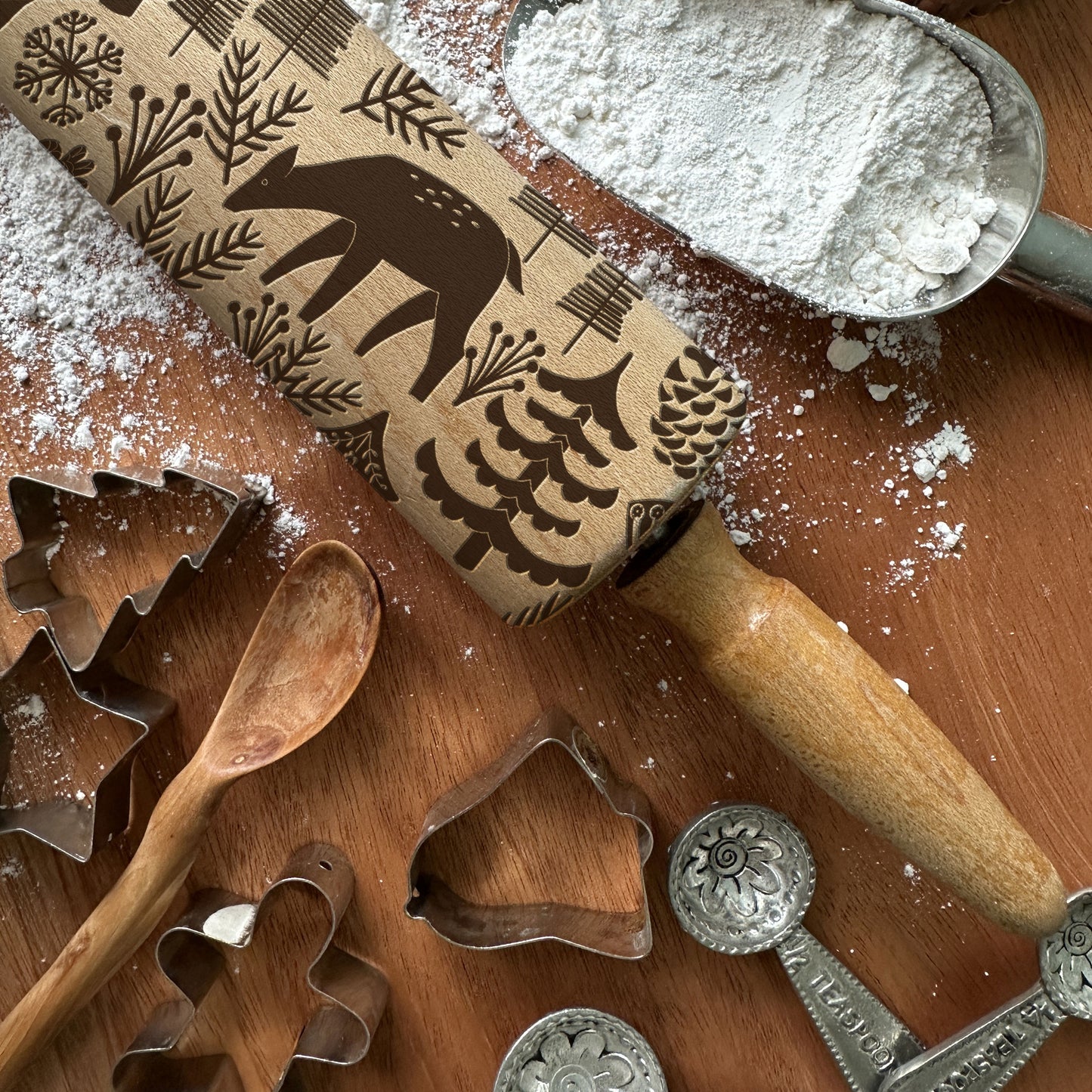 Wooden rolling pin with embossed designs on a wooden surface with flour and cookie cutters.