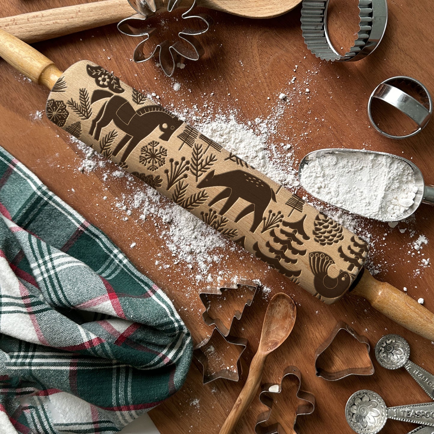 Rolling pin with embossed designs on a wooden surface with baking tools and flour.