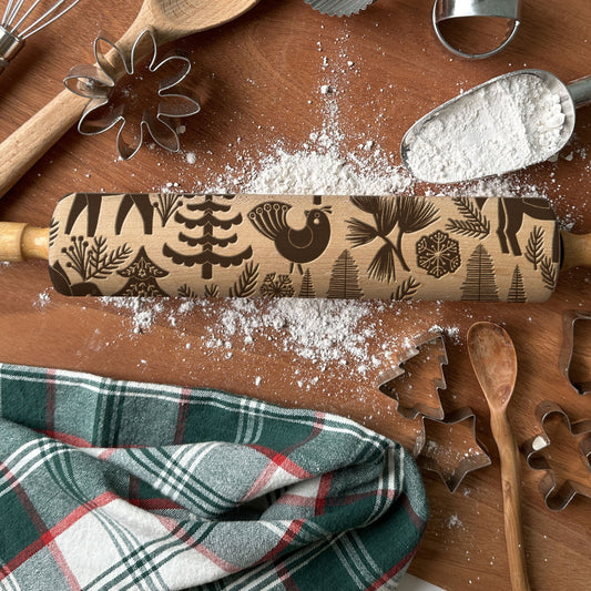 Wooden rolling pin with decorative patterns on a wooden surface with flour and baking tools.