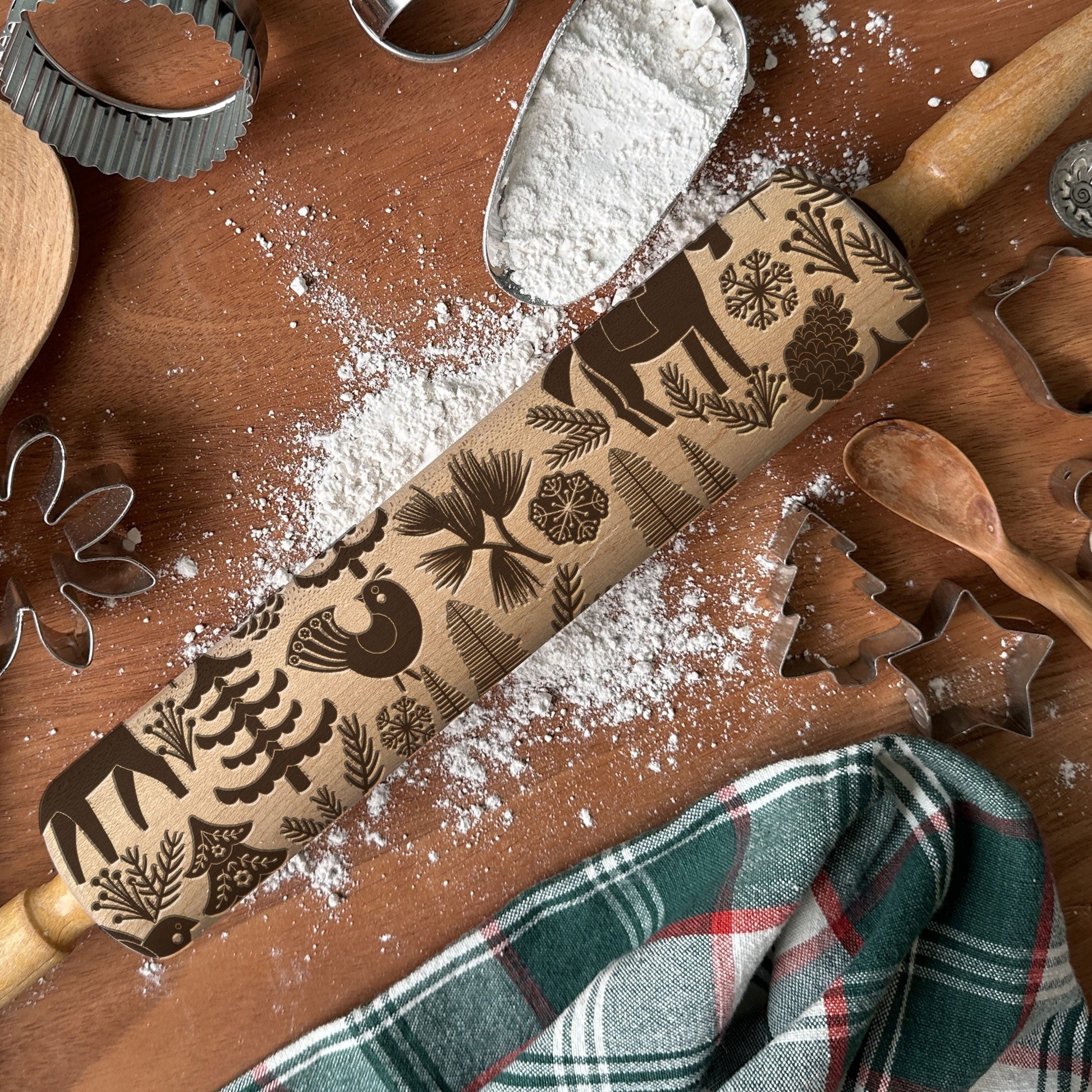 Wooden rolling pin with embossed designs on a wooden surface with flour and baking tools.