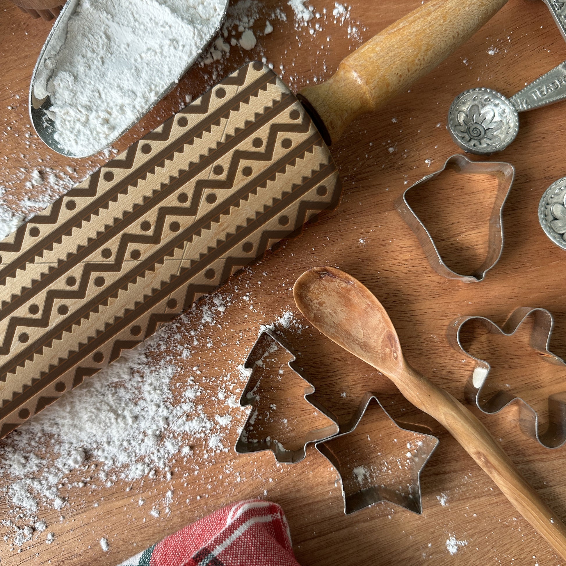 Wooden rolling pin with pattern, metal cookie cutters, and flour on a wooden surface.